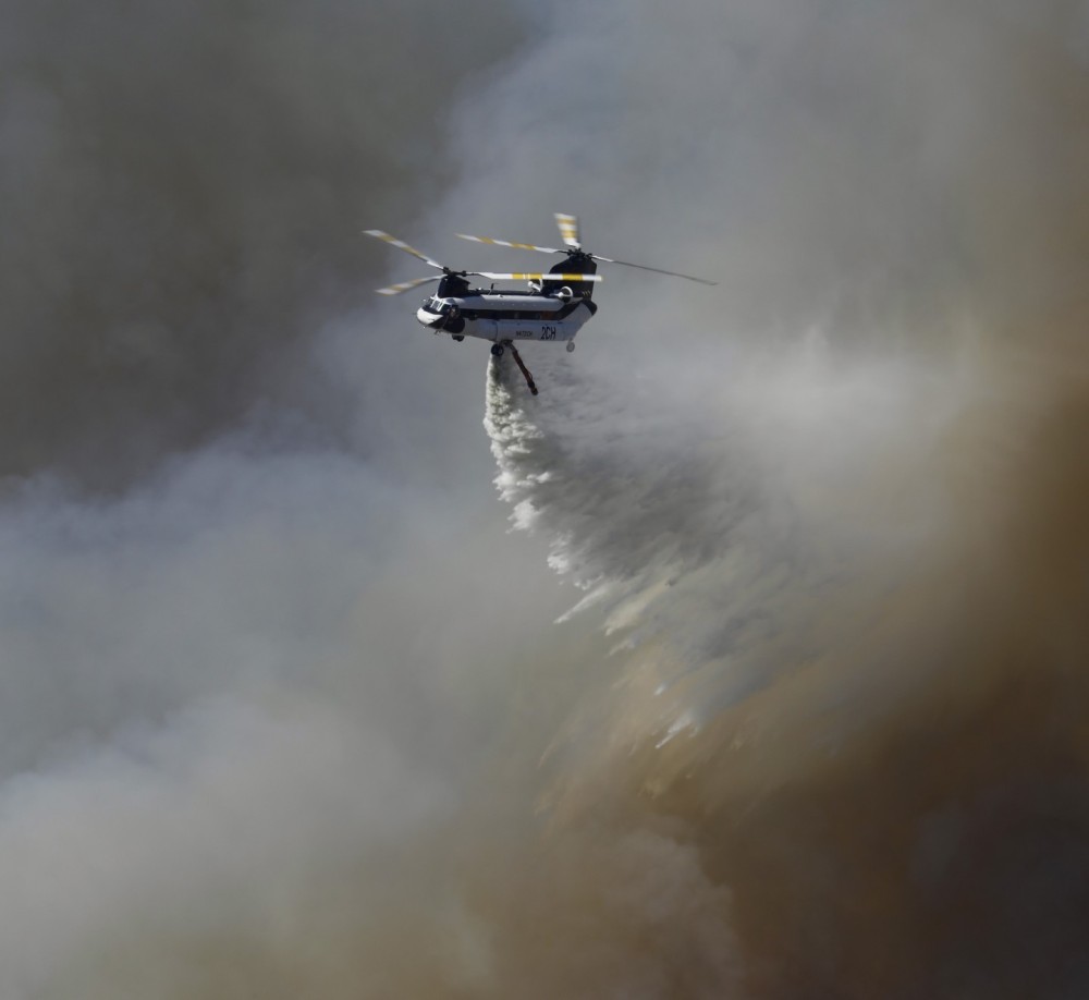 PJ Helicopters Helitanker 2CH passes through a smoke filled sky to deliver its 2,800 gallon payload on a large vegetation fire in Riverside County (CA) known as the Round Fire, in Summer 2024.