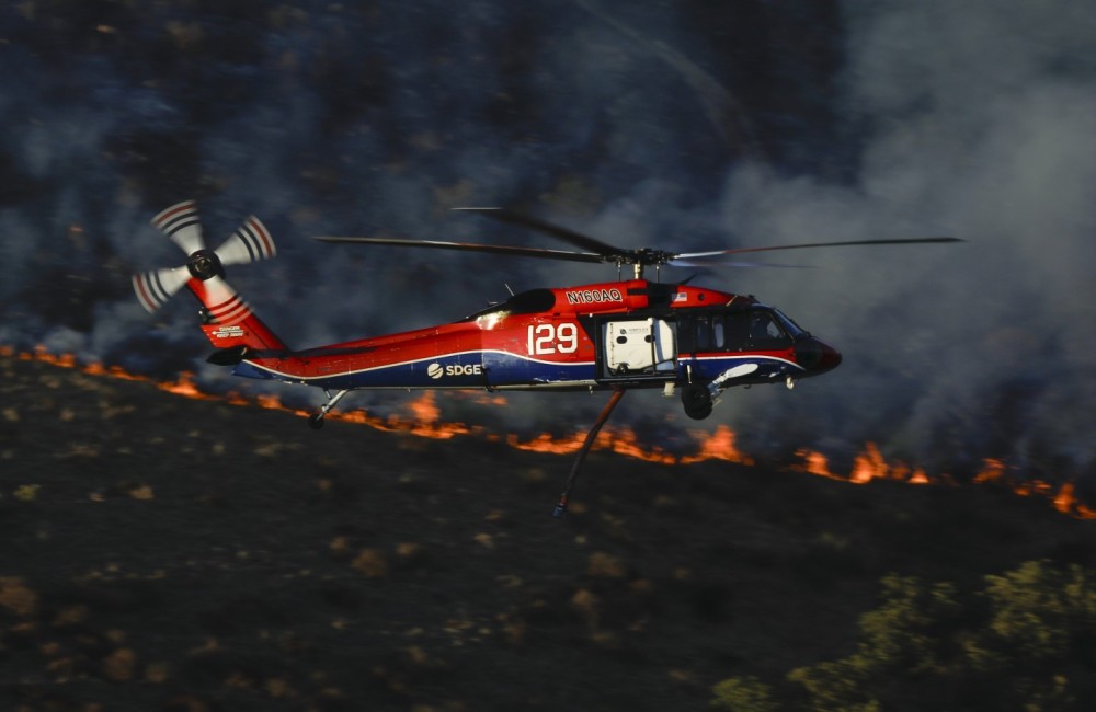 Copter 129, a Sikorsky UH-60A Black Hawk operated by the San Diego Gas & Electric power company in San Diego, CA, returns to the Border 77 Fire while passing a wall of fire in the Otay Mountain Wilderness of Otay, CA.