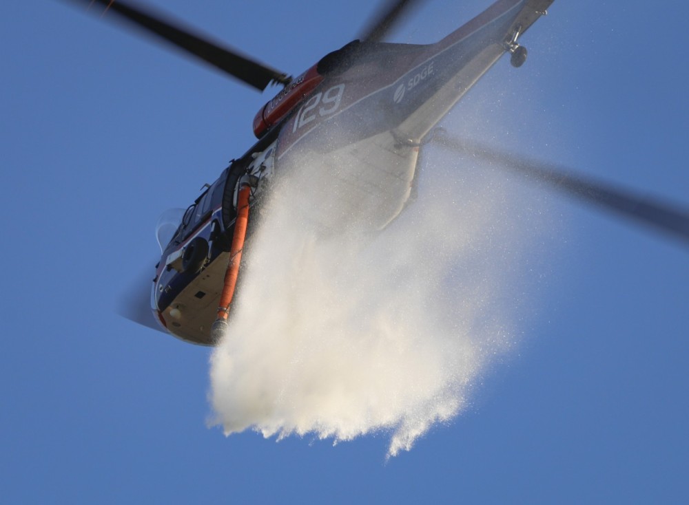 A UH-60 Black Hawk helicopter operated by the San Diego Gas & Electric power company, drops water on a midsized vegetation fire, caused by an arsonist in the area of Jamul, CA.