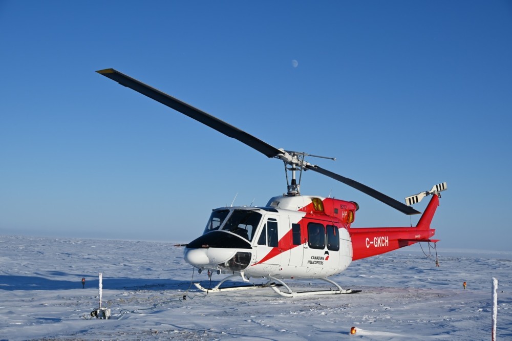 A Bell 212 HP rests on a pad near a radar site in the Canadian Arctic. During this time of year, in winter, the sun and the moon dance above us. The landscape resembles a lunar surface—a vast, white desert.