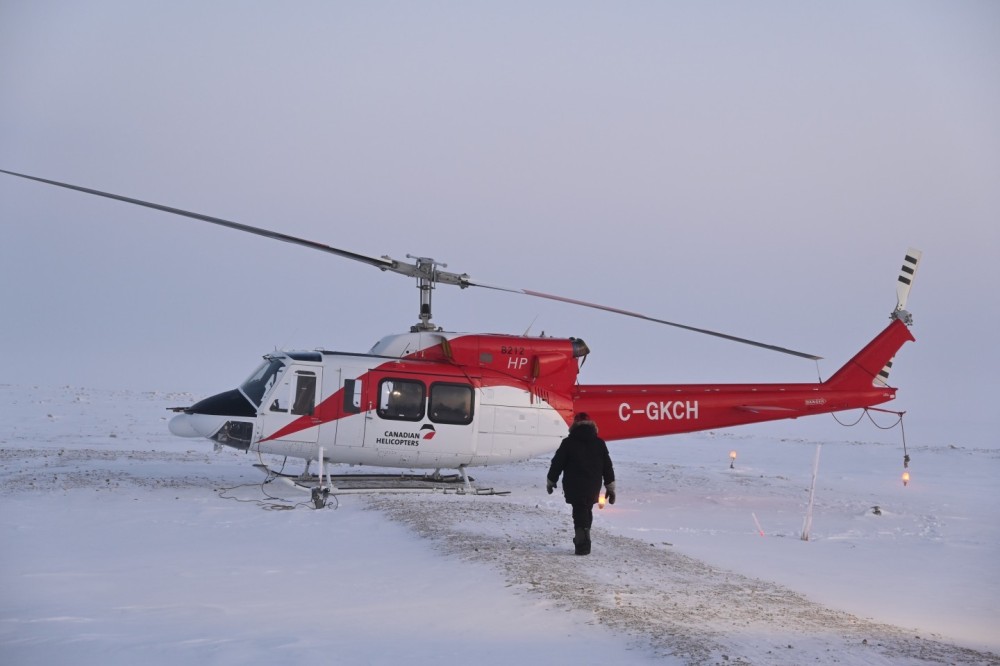 A Bell 212 HP rests on a pad near a radar site in the Canadian Arctic. My captain walks toward our helicopter, ensuring everything is ready for departure. It's near noon, yet the sun hangs low on the horizon. The temperatures are sub-zero, and preparing our aircraft with our winter gear is always a challenge.