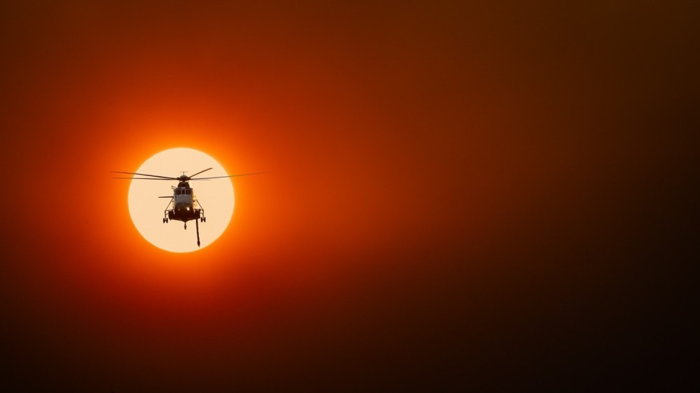 A Sikorsky S61N fire bomber returns to base after a long day on the Grampians Fire Grounds. The sun is smothered in thick bushfire smoke, creating a thick muddy scene, framing the helicopter in an apocalypse now type energy, not too dissimilar to the daily battle to overcome the flames and destruction that transpire below on a daily basis