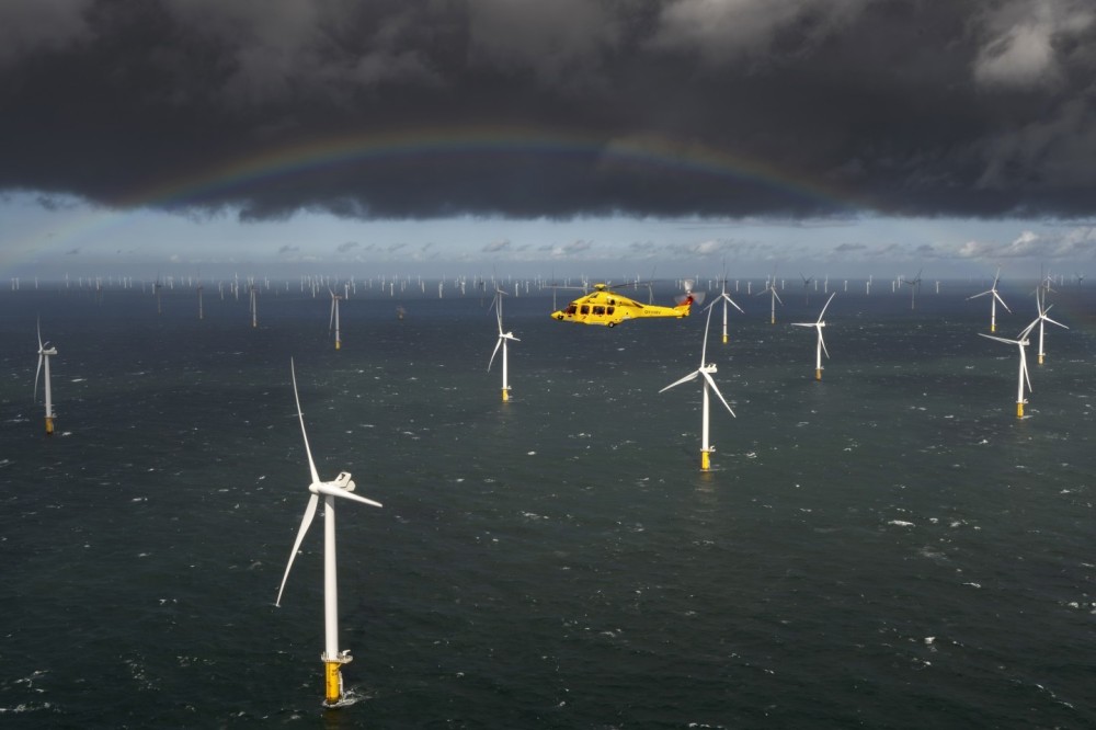 An air-to-air shoot featuring an Airbus H175 from Noordzee Helicopters Vlaanderen (NHV) above the North Sea, with a wind farm in the background and a beautiful rainbow adding to the stunning scene. Noordzee Helicopters Vlaanderen will expand its operations with the H175 into the offshore wind sector.