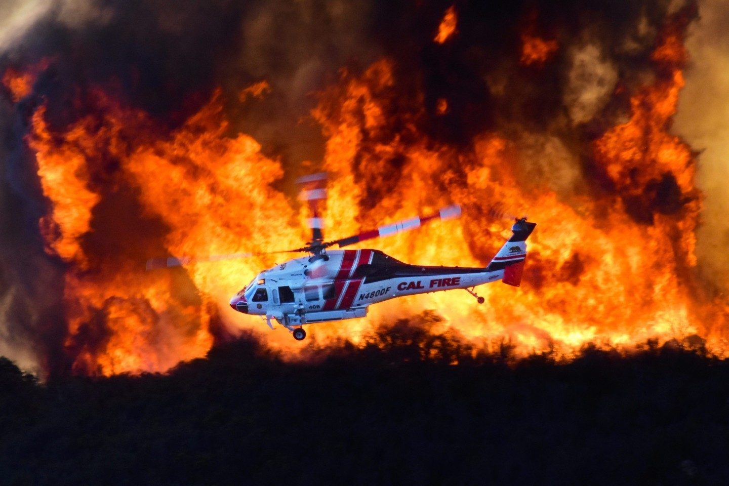 Cal Fire's Copter 406 comes out of the dipsite and crosses a wall of flame as they position themselves and look for the best place to drop their load of water.