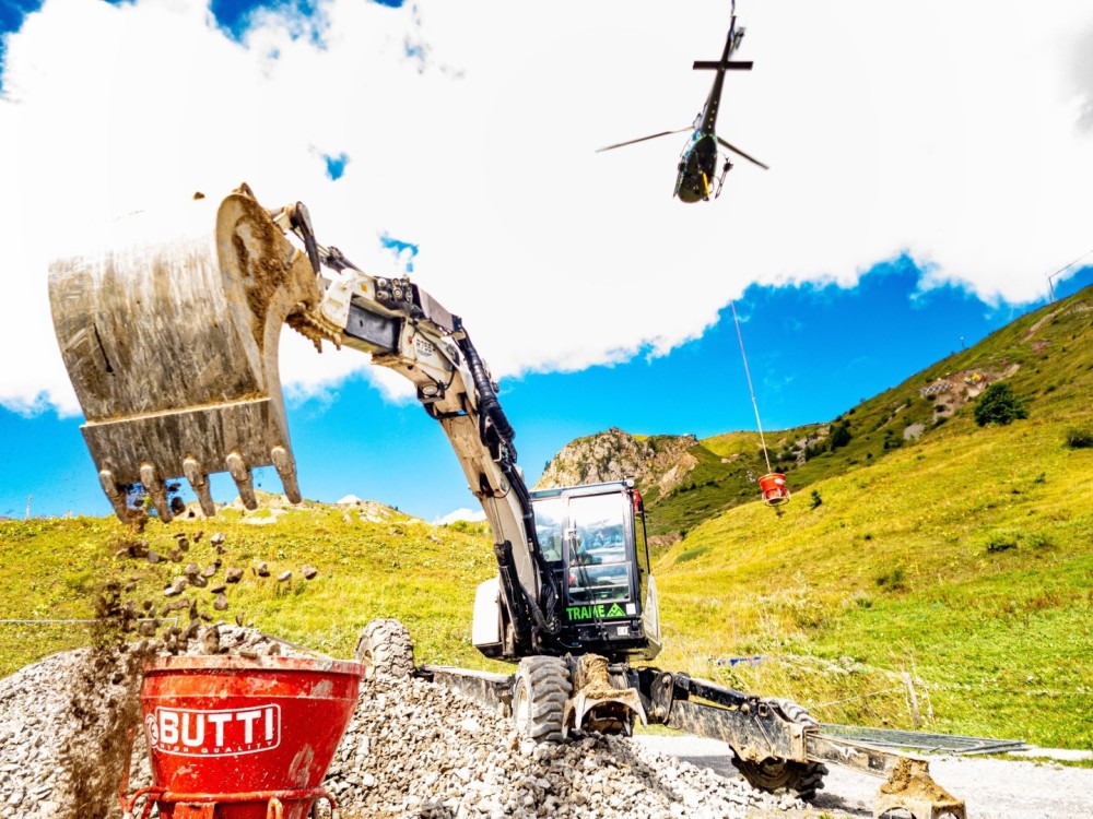 H125 of Savoie Hélicoptères compagny  working on transporting gravel with a spider excavator loading skips for ski lift work in the mountains with difficult access