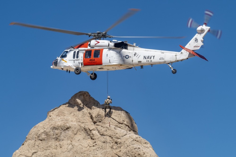 Naval Air Weapons Station China Lake Search and Rescue MH-60S Blackhawk practices out in the Southern California desert. A crew member is lifted up along a rock formation as the skilled pilots hover above.