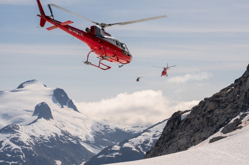 Three TEMSCO helicopters AS350s departing a dog sledding camp high up on the Mendenhall glacier on a beautiful Alaskan day. Background is mount stroller white.