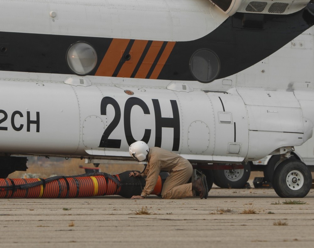 PJ Helicopters Boeing CH-47D Chinook operating as Helitanker 2CH assigned to the massive Line Fire in Highlands, CA, a crew chief checks the underbelly of the aircraft during start-up procedures at the Redlands Airport in Redlands, CA.