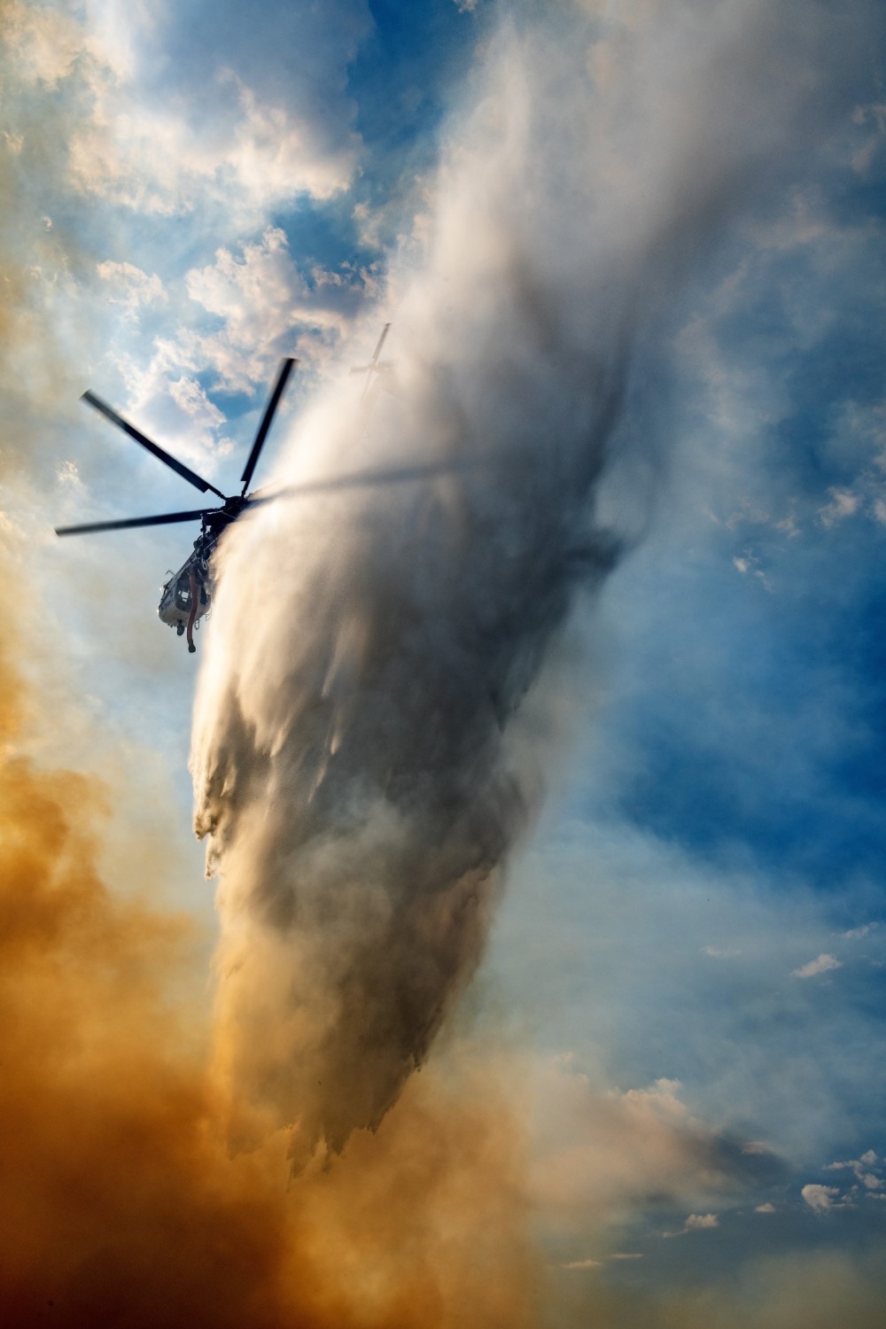 I was at the Record Fire on a road where the fire was on both sides.  I watched where the helicopters were dropping water and I drove a little way up the road, hopefully to put myself in the correct location. I put on my Nikon 24mm to 70mm lens and started shooting when Helicopter Transport Services, Skycrane flew over. I have to say the overspray of the water landing on me was very refreshing because I was in my full fire gear and the temperature was over 100°.