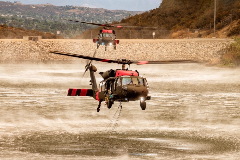 Two Los Alamitos National Guard Blackhawk helicopters, 830 and 831, pick up water from the Crafton Hills Reservoir in Yucaipa, California to dump on the Line Fire. I positioned myself on a hill above the reservoir for the best angle and to clear the fence that was around it. The sun was diffused by smoke clouds which made the light very warm.