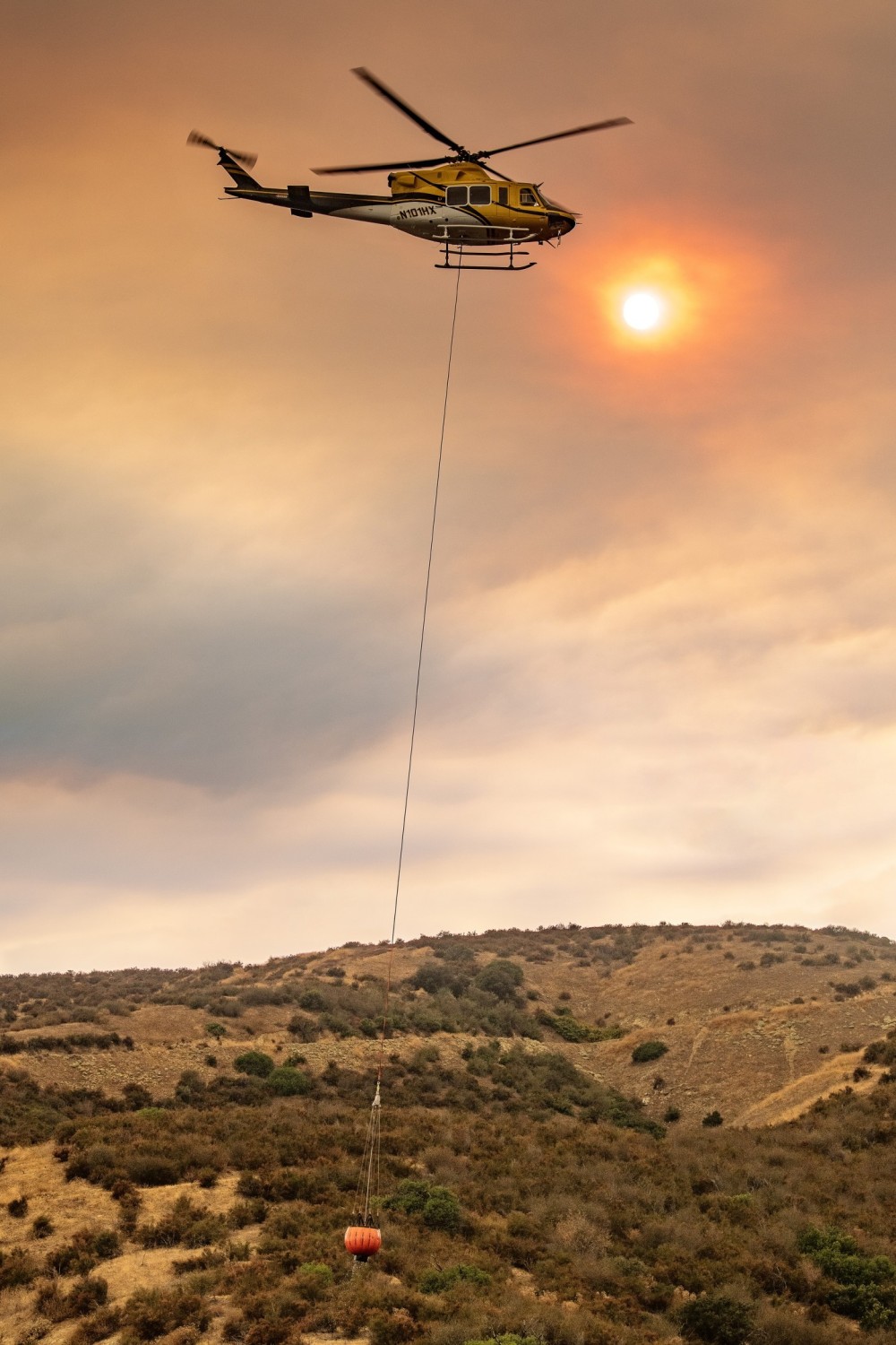 Helicopter Express’s Bell Textron 412 picks up water from Crafton Hills Reservoir on its way to the Line Fire in the San Bernardino Mountains. I saw that it was going to pass by the sun, diffused by the smoke from the fire, so I turned my camera vertical to include the Bambi Bucket.